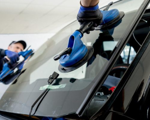 Automobile special workers replacing windscreen or windshield of a car in auto service station garage.